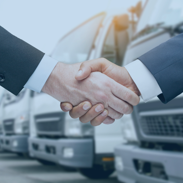 Two businessmen shaking hands in front of trucks.